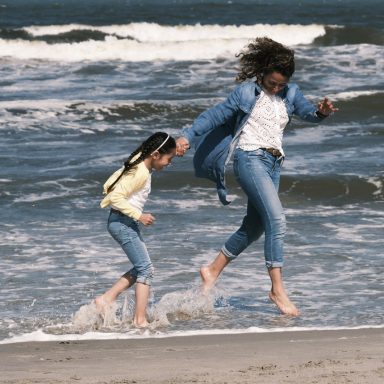 Gezinsfotoshoot op het strand van Den Haag Een moeder en dochter rennen lachend door het water op het strand.