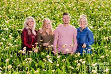 Familiefotoshoot in De Lier Groep van vier mensen, staand in een veld vol bloemen, met glimlachen en verschillende kledingstijlen.