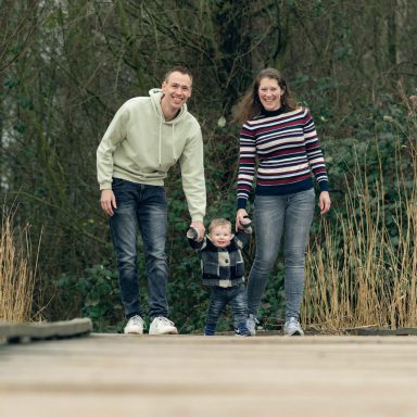 Winterse fotoshoot in Vlaardingen Een jonge familie wandelt samen op een houten pad in de natuur.