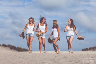 Vriendinnen fotoshoot op het strand in zuid-holland Vrouwelijke vrienden wandelen met blote voeten op het strand, lachend en met hoeden.