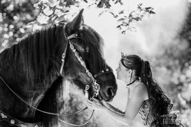 Fotoshoot met paard Vrouw met lange haren kijkt liefdevol naar een zwart paard in een bosachtige omgeving.