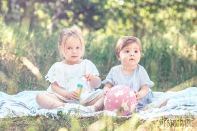 Fotoshoot Meijendel in Wassenaar Twee jonge kinderen zitten op een deken in een groene, zonovergoten omgeving.