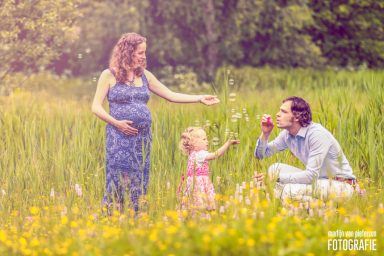 Zwangerschapsfotoshoot met bellenblaas Zwangerschapsfoto van een gezin in een bloeiend veld met een kind en een man.