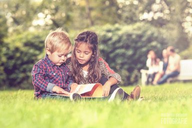 Fotoshoot Park Overvoorde in Rijswijk Twee kinderen zitten op het gras en lezen samen een boek in een park.