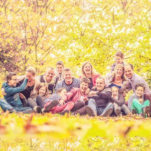 Fotoshoot in de herfst met familie in Delftsche Hout. Groep van mensen zittend op de grond in een herfstlandschap met kleurrijke bladeren.