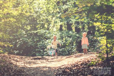 Fotoshoot Ockenburgse bos Twee kinderen spelen op een pad in een bos met groene bomen en zonlicht.