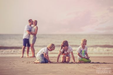 Fotoshoot op het strand Kinderen spelen op het strand terwijl een stel elkaar omarmt op de achtergrond.