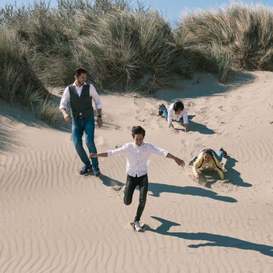 Fotoshoot in de duinen van Hoek van Holland Een man en drie kinderen spelen op een zandstrand, met duinen op de achtergrond.
