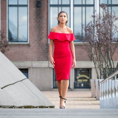 Fotoshoot met Janice Blok in Rotterdam Vrouw in een rode off-shoulder jurk, lopend tussen moderne architectuur in Rotterdam.