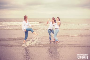 Fotoshoot aan zee in Kijkduin Drie vrouwen lachen en spelen in de branding op het strand.