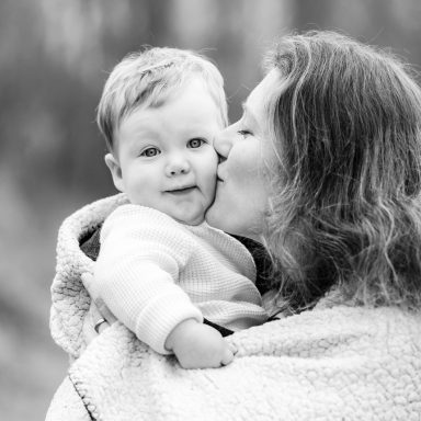 Fotoshoot in de winter in Vlaardingen Zwartwit foto van een moeder die haar lachende baby kust.