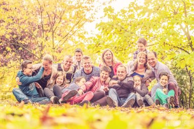 Fotoshoot in de herfst in Delft Een grote groep mensen, lachend en zittend op de grond tussen herfstbladeren.