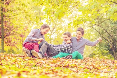 Fotoshoot in de herfst in Delft Drie kinderen spelen op een bed van bladeren in een herfstlandschap.