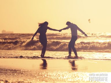 Fotoshoot bij zonsondergang Een silhouet van een stel dat hand in hand over het strand loopt bij zonsondergang.