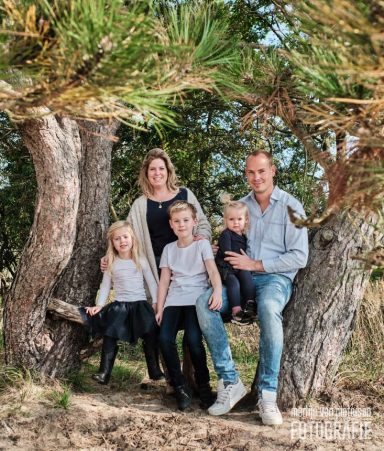 Fotoshoot in het Westduinpark in Den Haag Gezin met twee volwassenen en drie kinderen, zittend tussen bomen in de natuur.