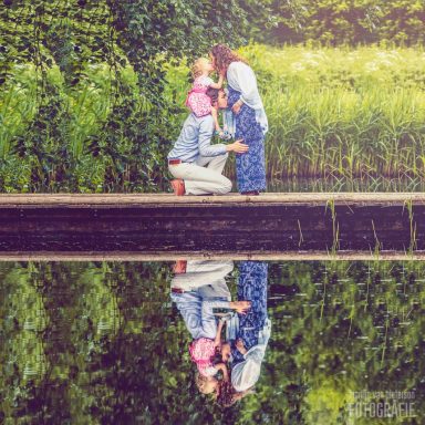 Zwangerschapsfotoshoot in Delft Een stel staat op een oever, terwijl ze elkaar liefdevol aankijken en hun reflectie in het water zien.