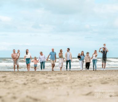 Familiefotoshoot op het strand van 's-Gravenzande Groep mensen wandelt langs het strand met de zee op de achtergrond.